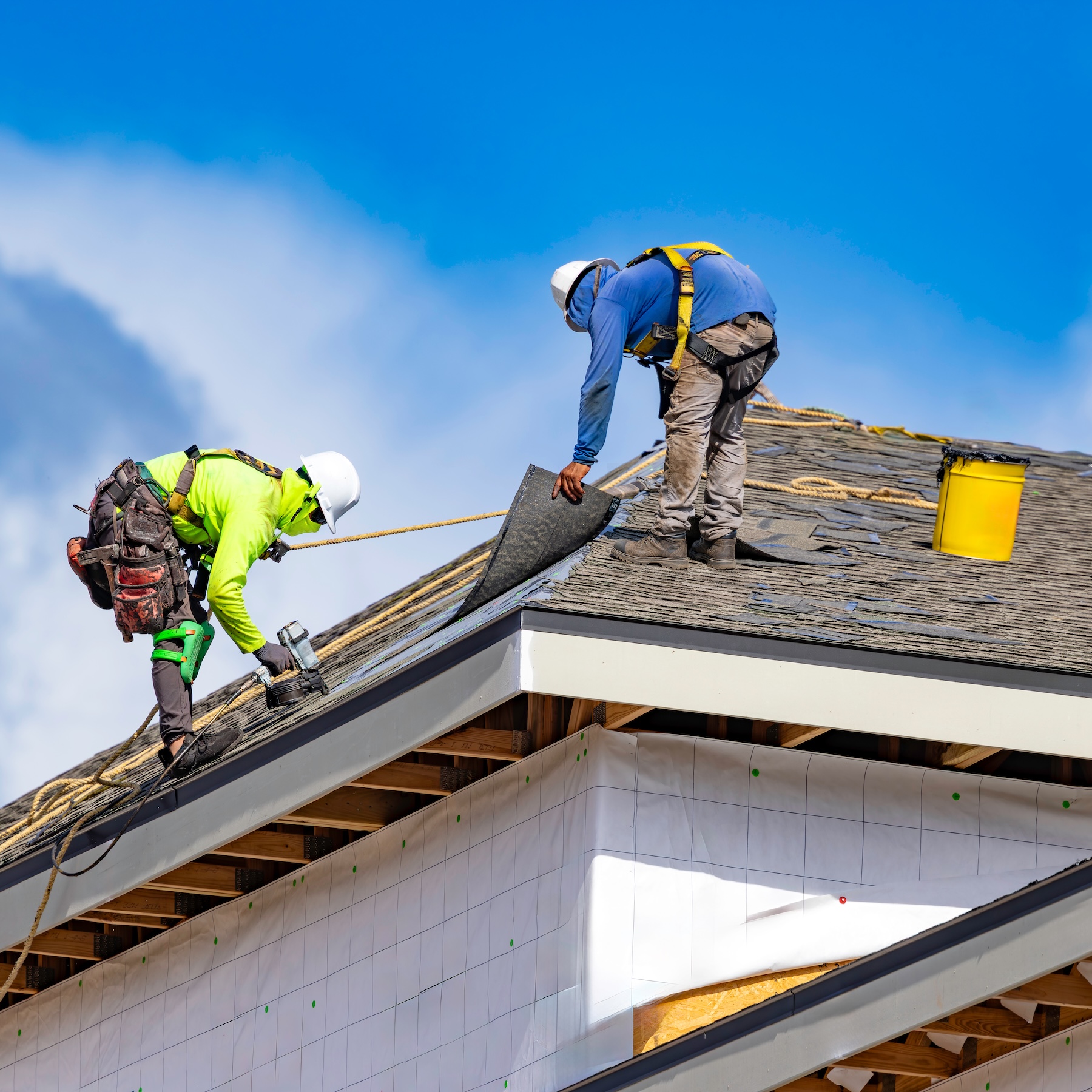 Roofing contract workers replacing shingles on second story roof